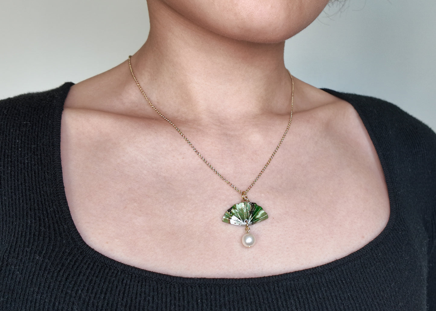 A gold-colored origami fan necklace with a faux pearl drop on a model