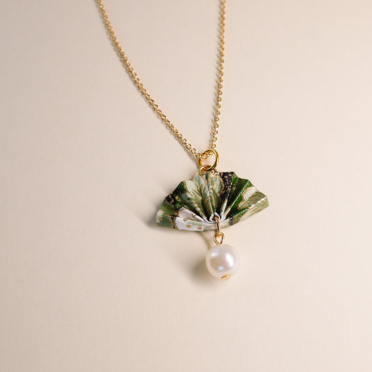 A gold-colored origami fan necklace with a faux pearl drop on a light background. handmade with green japanese paper