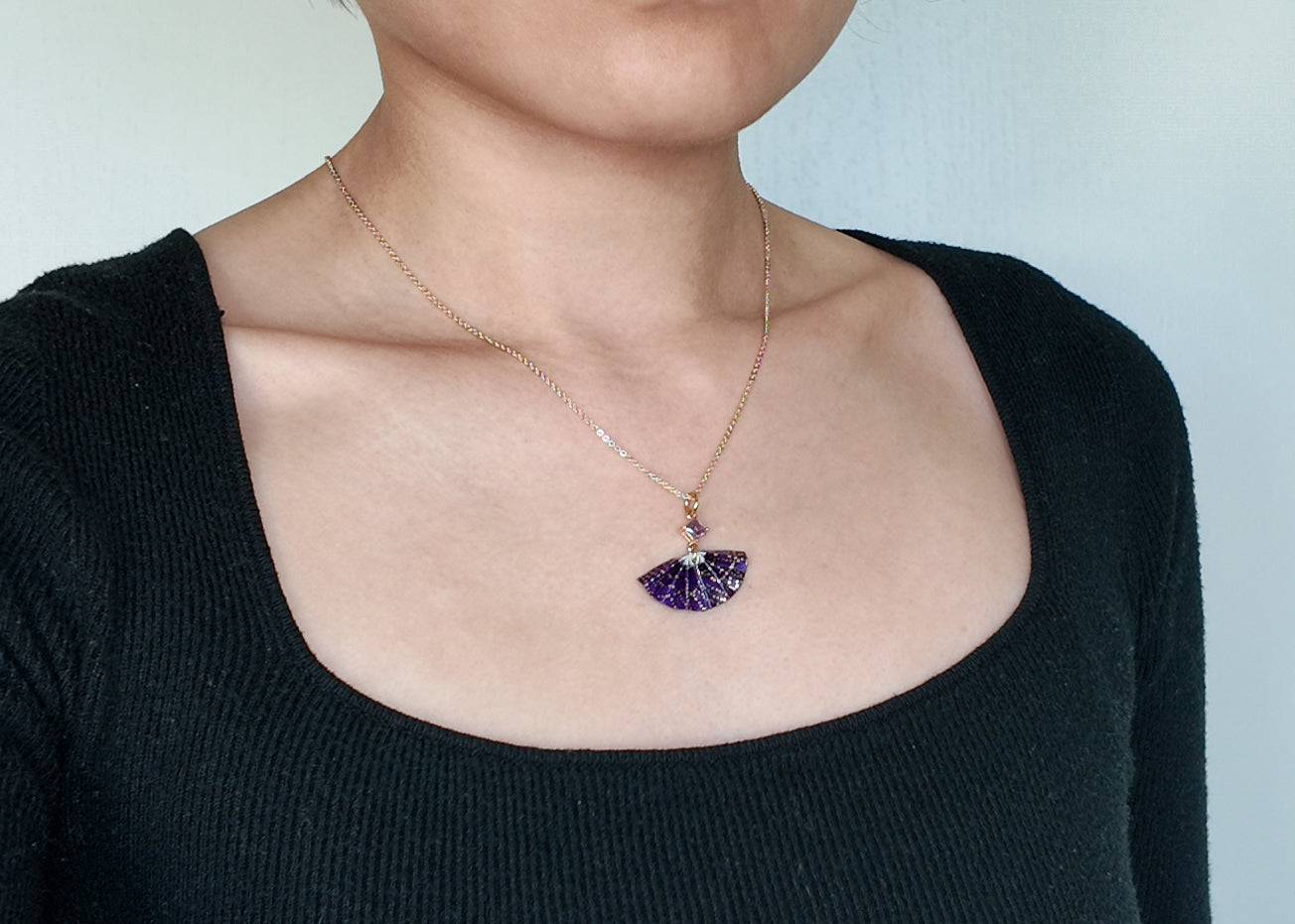 gold color necklace with purple origami fan pendant on a model