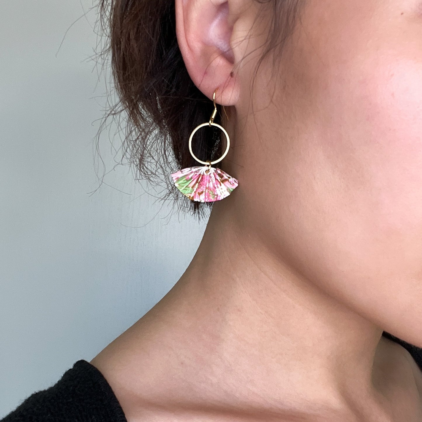 A pair of origami fan earrings with gold-colored hoops and cherry blossom paper fans, displayed on a human model