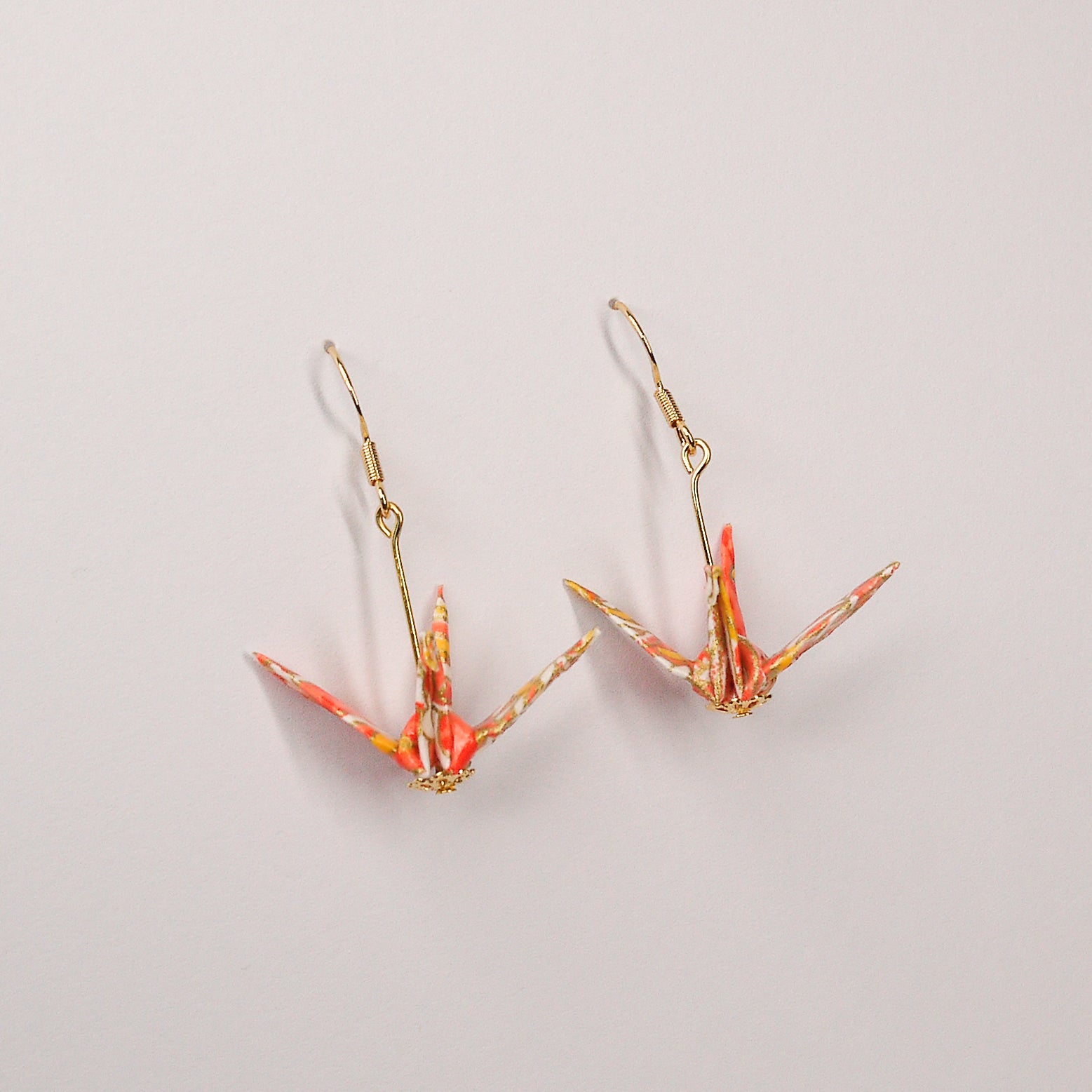 Pair of handmade orange origami crane earrings with chrysanthemum floral print and gold hooks, crafted from traditional Japanese washi paper. side view
