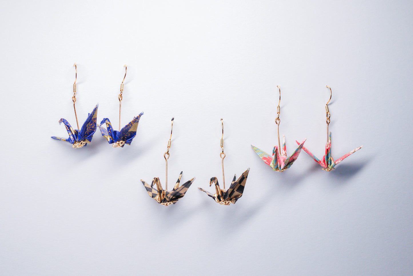 Collection of handmade origami crane earrings in various colors, featuring gold hooks and delicate paper cranes crafted from traditional Japanese washi paper.