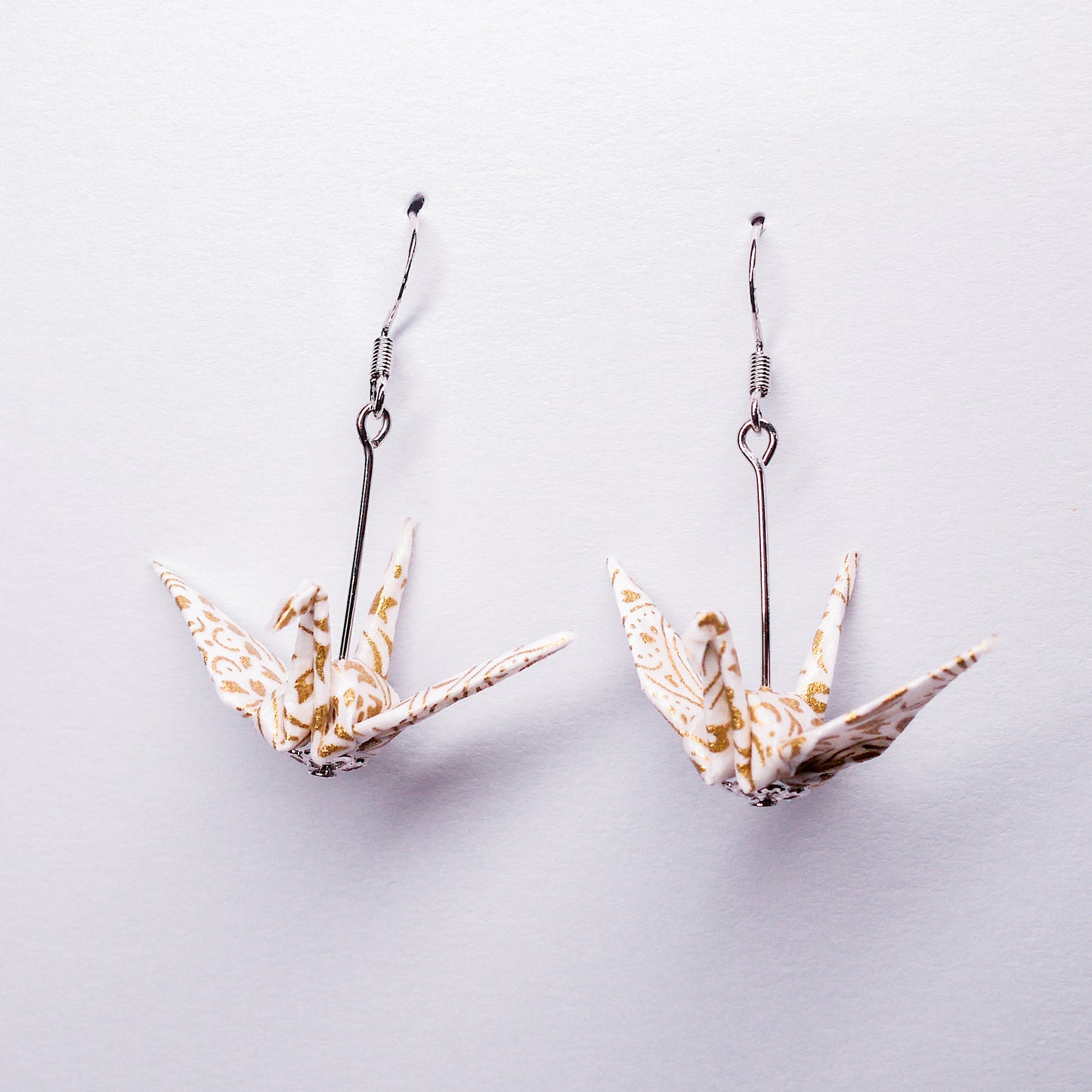 Pair of handmade white origami crane earrings with gold flower prints and hooks, crafted from traditional Japanese washi paper. front view