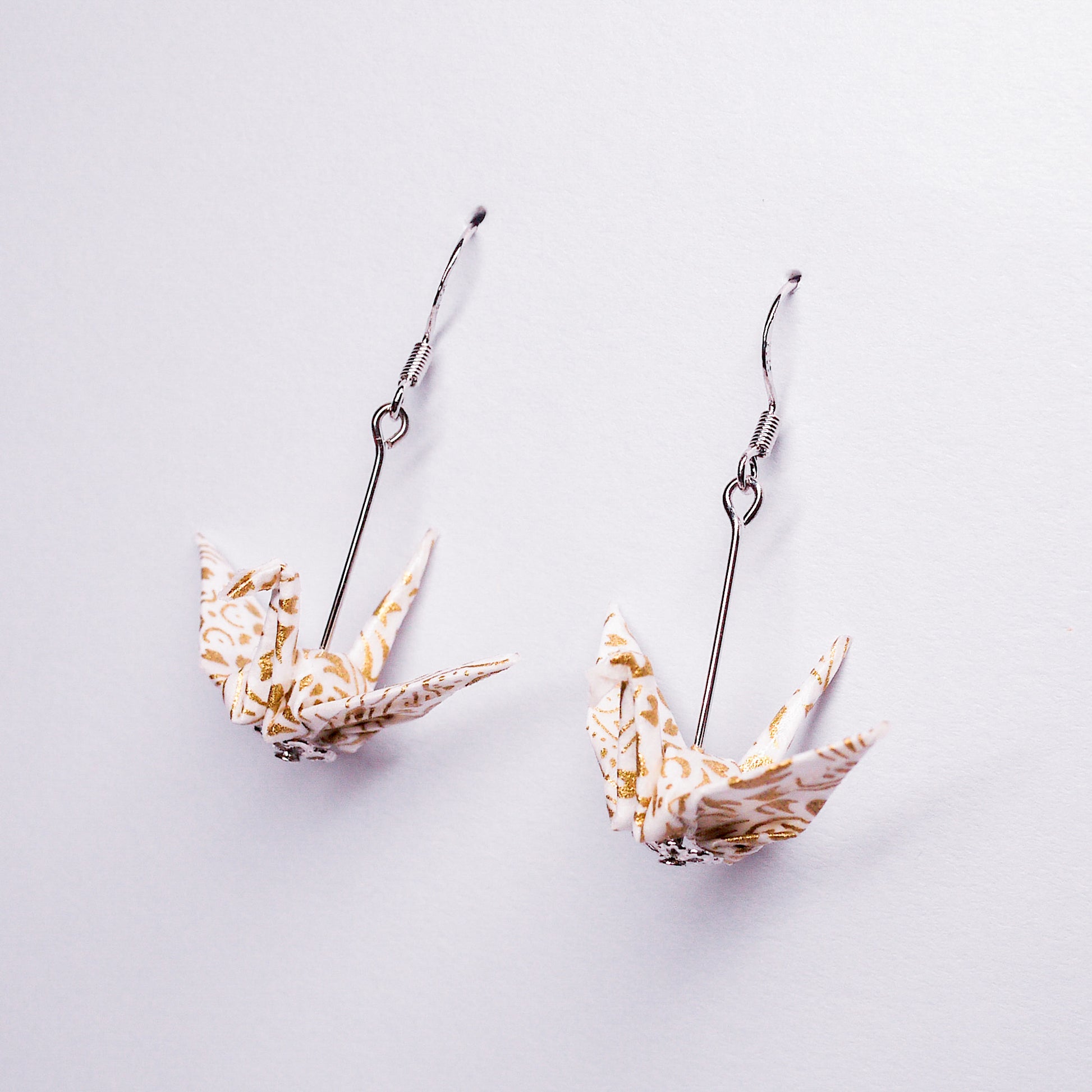 Pair of handmade white origami crane earrings with gold flower prints and hooks, crafted from traditional Japanese washi paper. side view