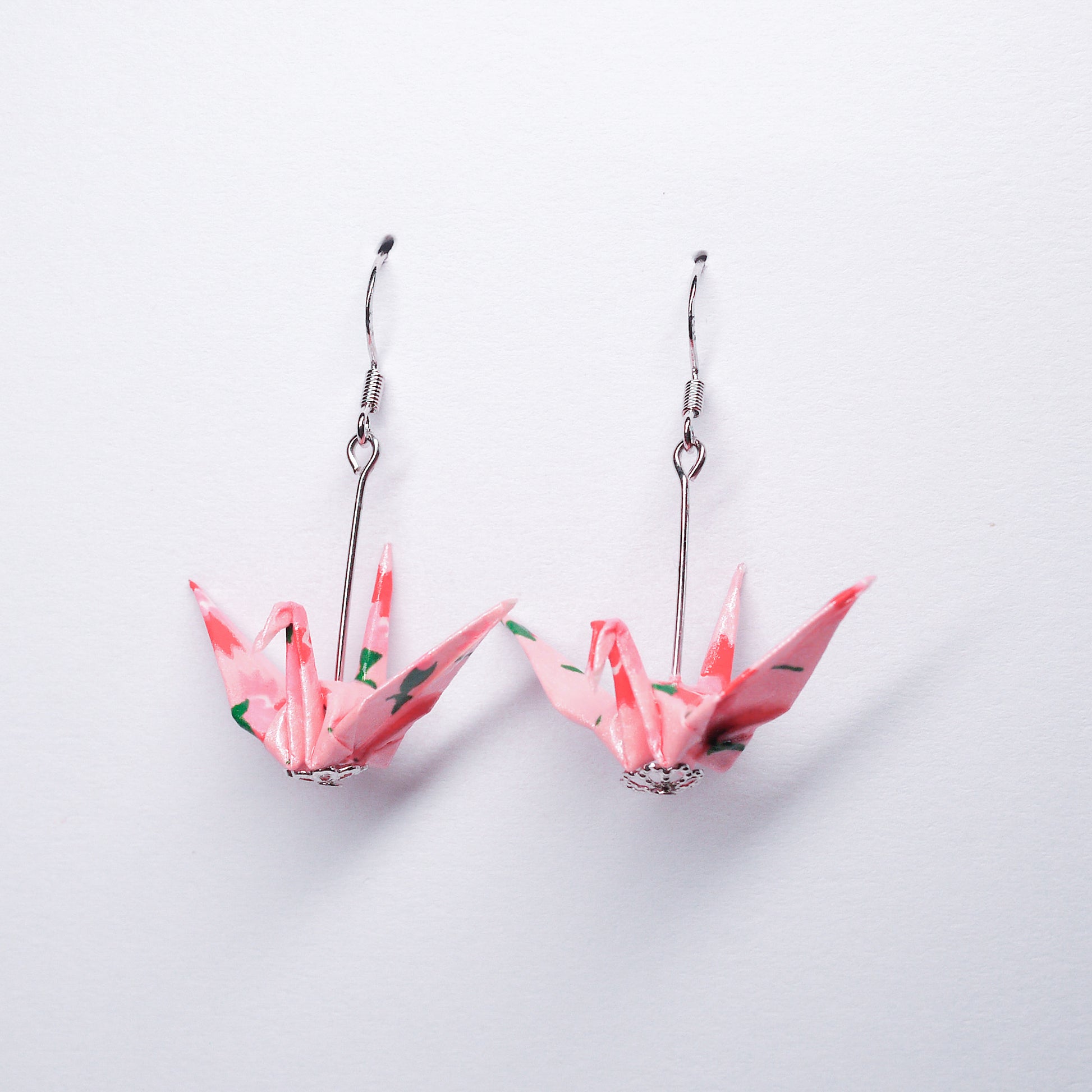 Pair of handmade pink origami crane earrings with pink flower prints and hooks, crafted from traditional Japanese washi paper. front view