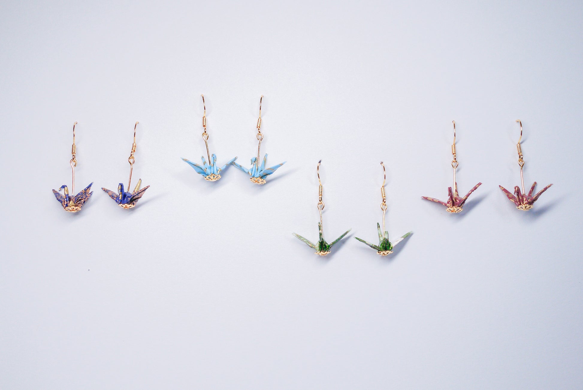 Collection of handmade origami crane earrings in various colors, featuring gold hooks and delicate paper cranes crafted from traditional Japanese washi paper