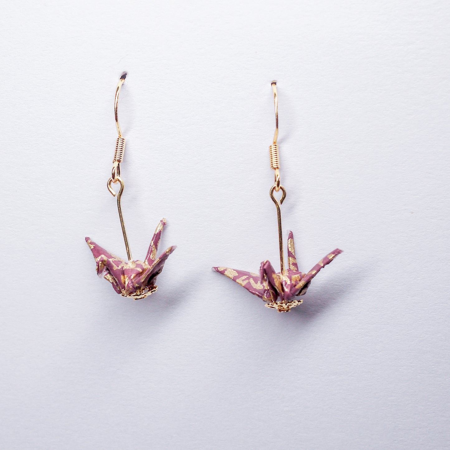 Pair of handmade purple origami crane earrings with gold flower prints and hooks, crafted from traditional Japanese washi paper. front view