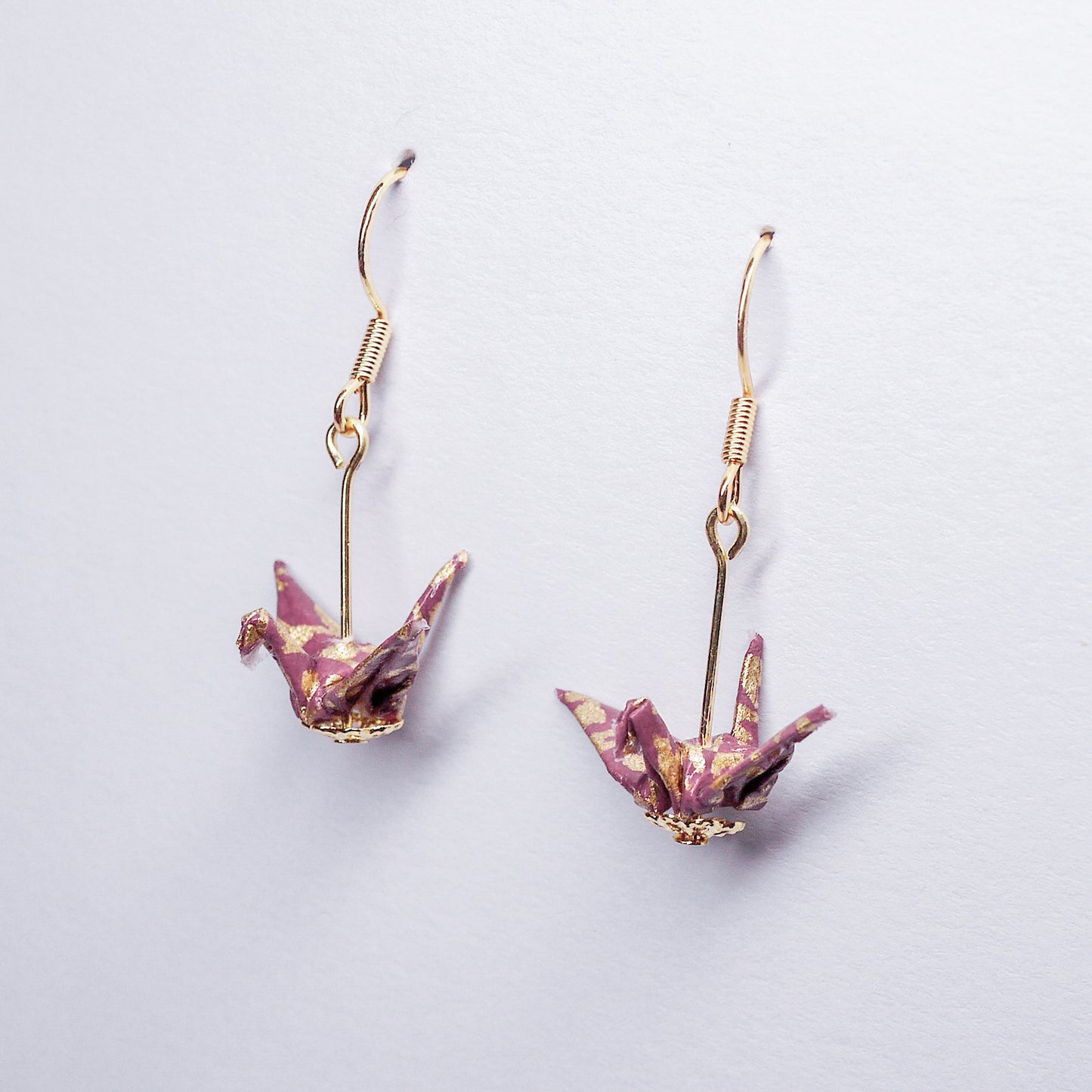 Pair of handmade purple origami crane earrings with gold flower prints and hooks, crafted from traditional Japanese washi paper. side view