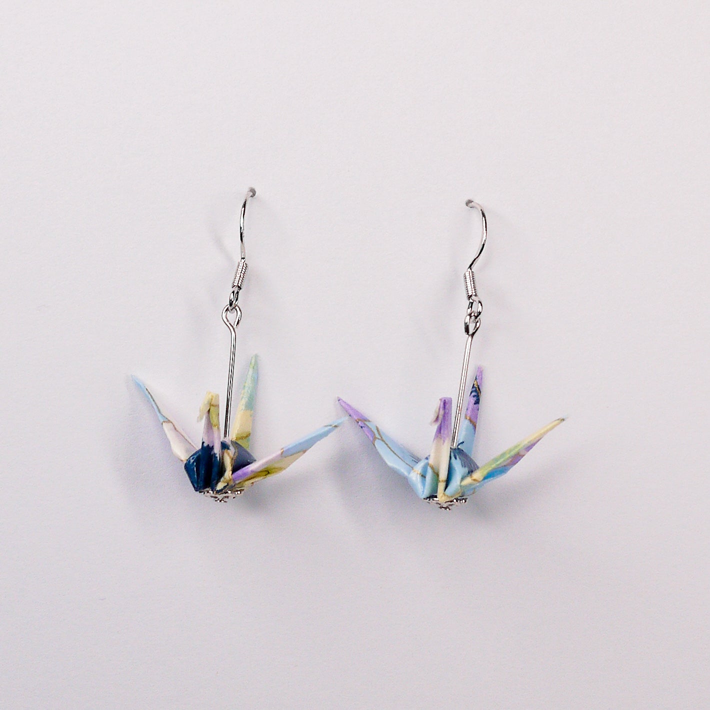 Pair of handmade purple and blue origami crane earrings with pansy floral print and silver hooks, crafted from traditional Japanese washi paper. front view