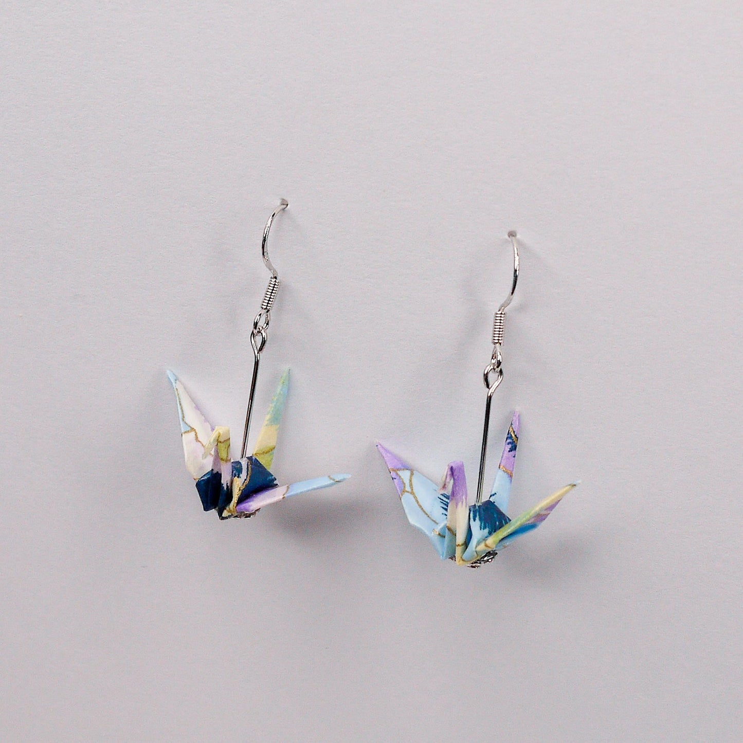 Pair of handmade purple and blue origami crane earrings with pansy floral print and silver hooks, crafted from traditional Japanese washi paper. side view