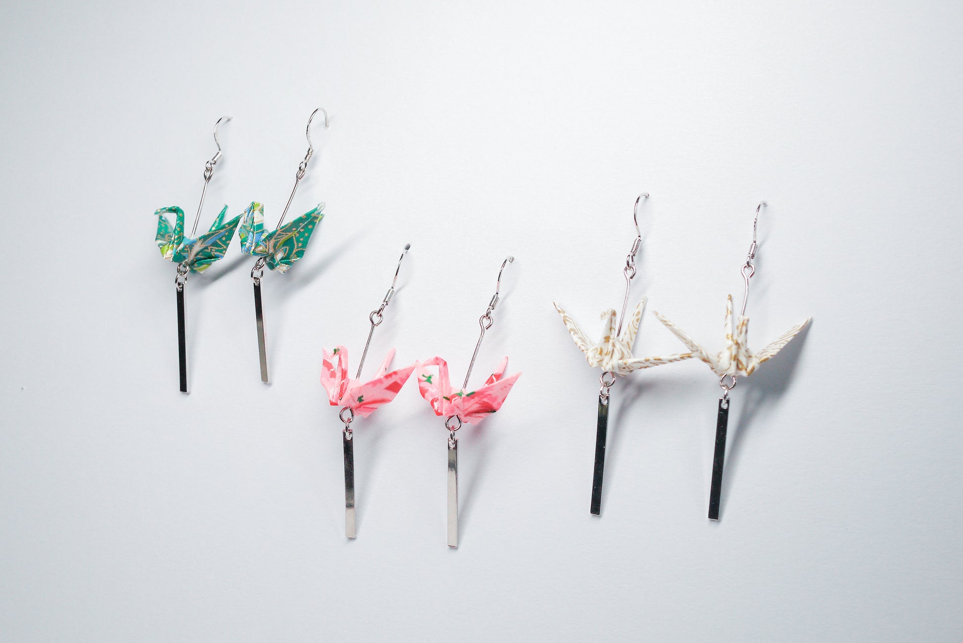 Collection of handmade origami crane earrings in various colors, featuring gold hooks and delicate paper cranes crafted from traditional Japanese washi paper.