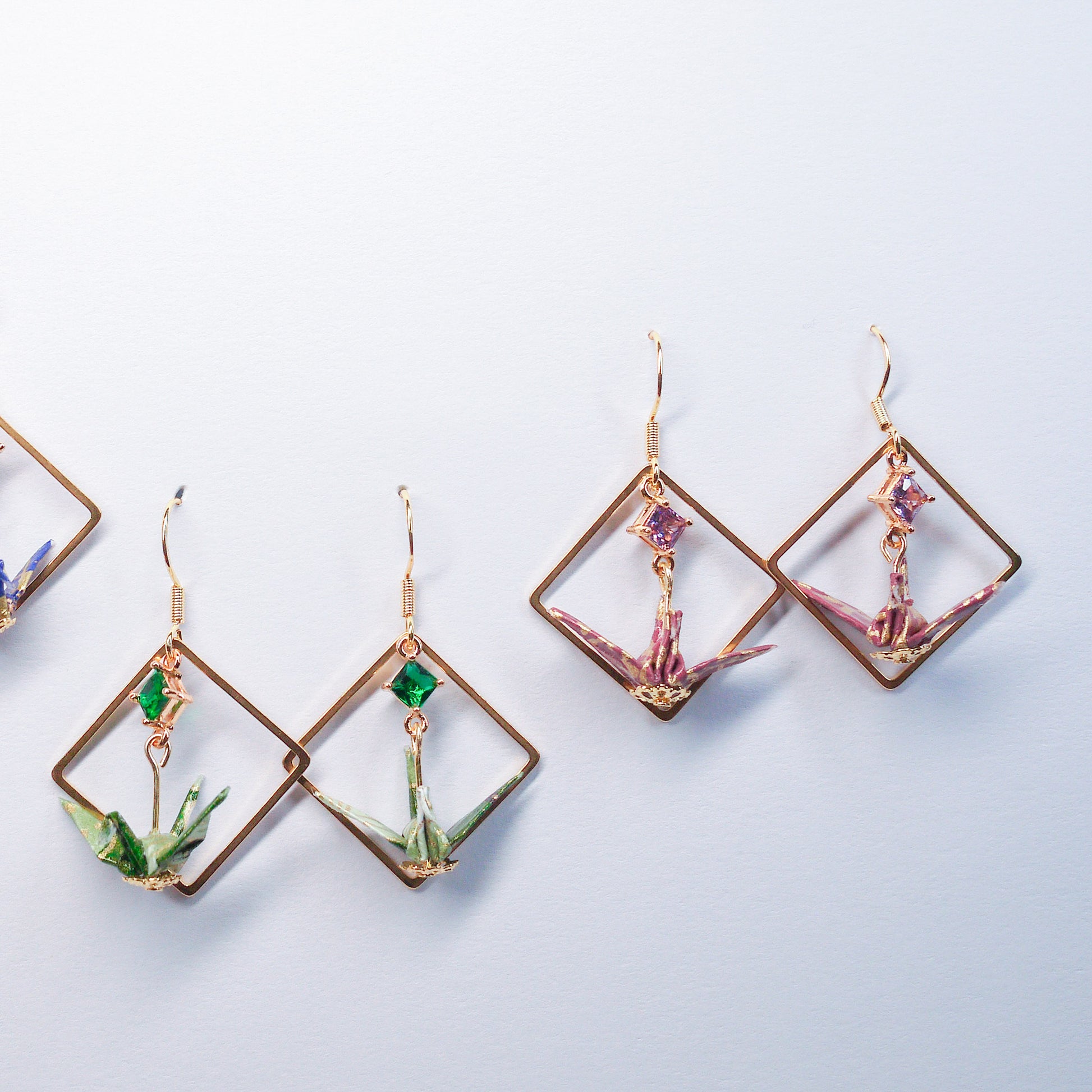 Collection of handmade origami crane earrings in various colors, featuring gold hooks and delicate paper cranes crafted from traditional Japanese washi paper.