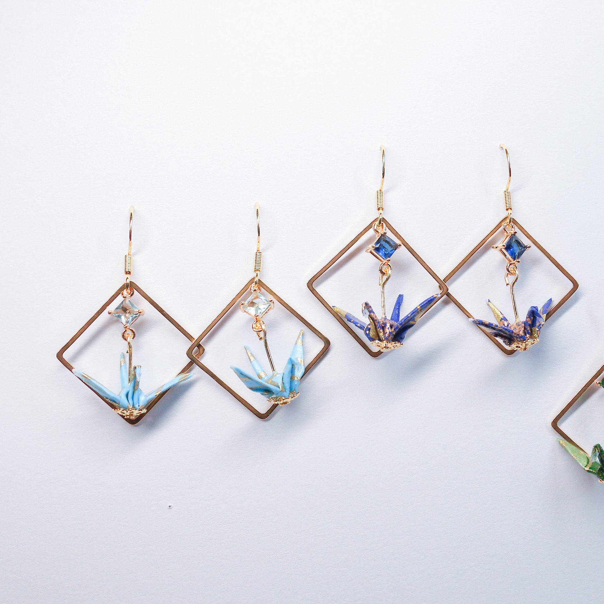 Collection of handmade origami crane earrings in various colors, featuring gold hooks and delicate paper cranes crafted from traditional Japanese washi paper.