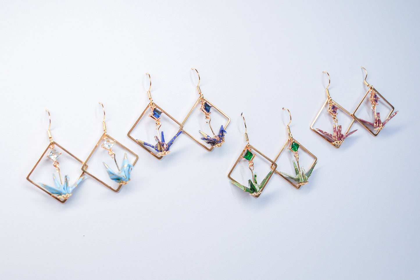 Collection of handmade origami crane earrings in various colors, featuring gold hooks and delicate paper cranes crafted from traditional Japanese washi paper.