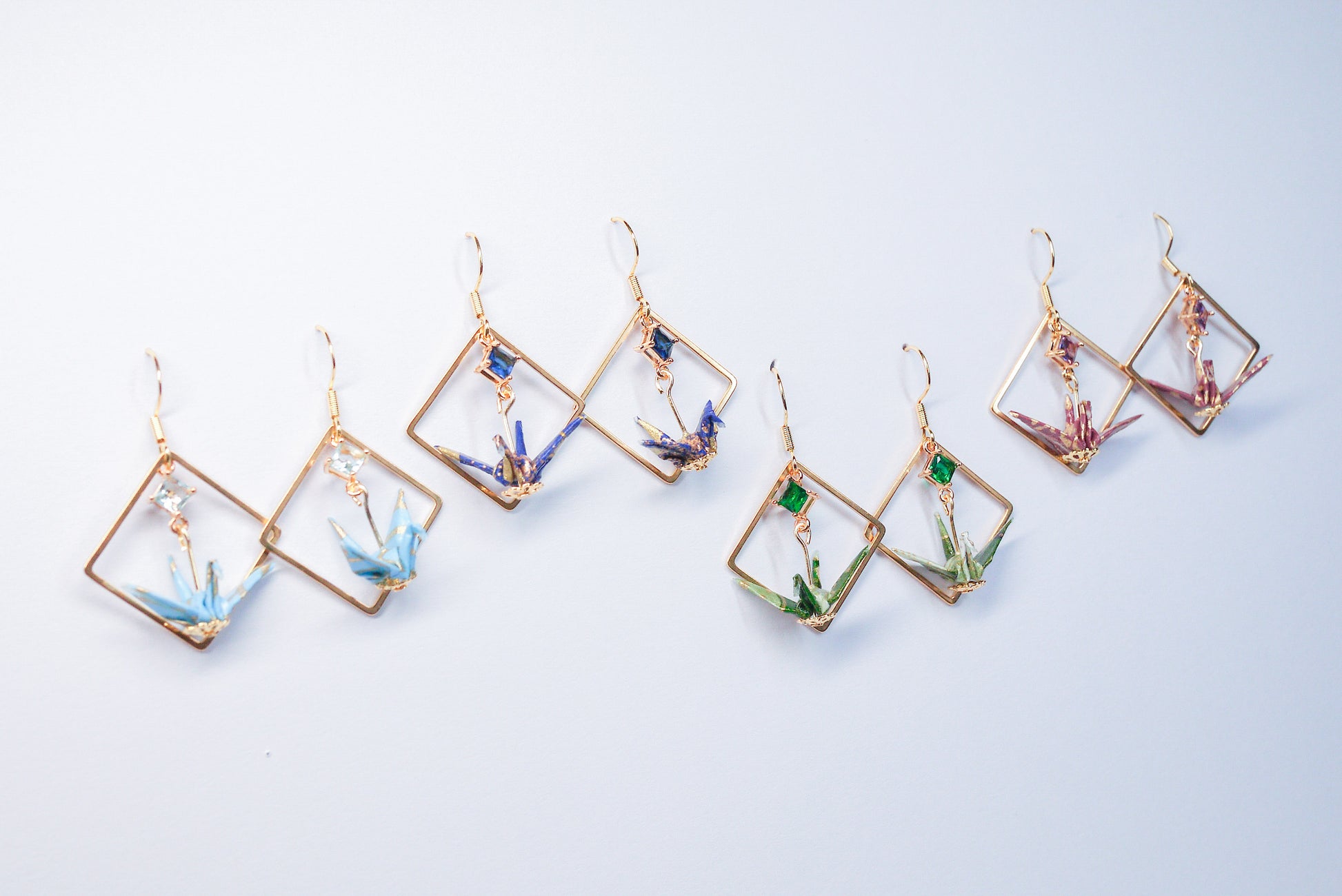 Collection of handmade origami crane earrings in various colors, featuring gold hooks and delicate paper cranes crafted from traditional Japanese washi paper.