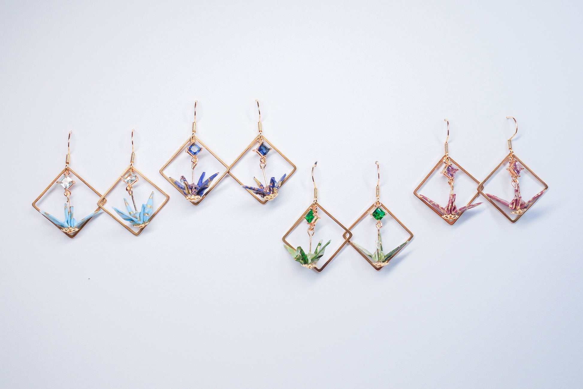 Collection of handmade origami crane earrings in various colors, featuring gold hooks and delicate paper cranes crafted from traditional Japanese washi paper.