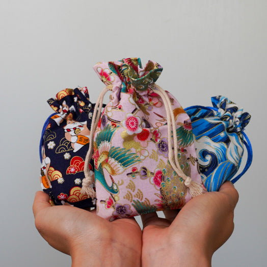 Three colorful drawstring bags held in a hand against a plain background